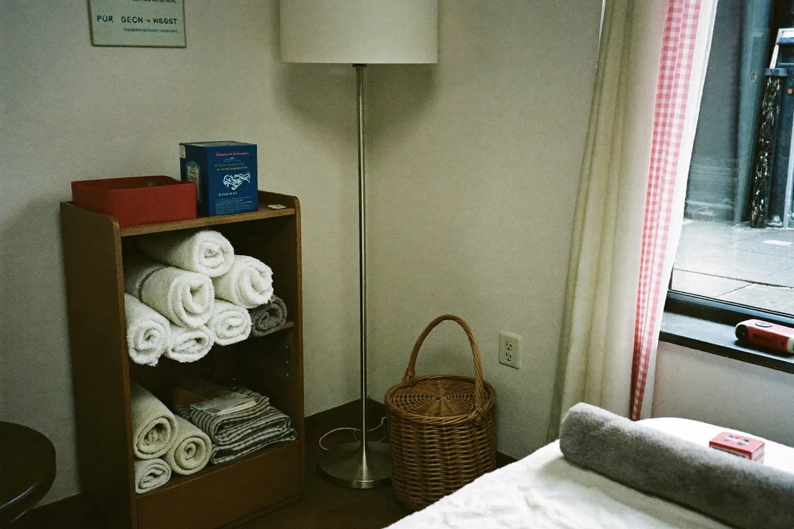 A corner of the treatment room with rolled towels, a basket and a curtained window
