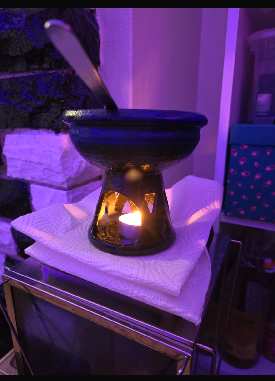 Candle-lit wax warmer and spatula resting on folded white towels in the treatment room